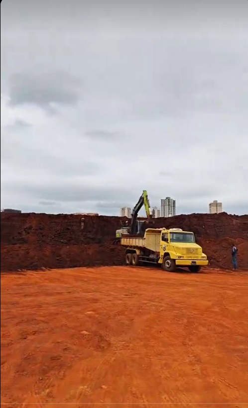 Escavadeira ao lado de caminhão basculante em terreno de terra vermelha